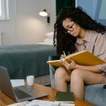 a young woman writing in a notebook while sitting on a couch